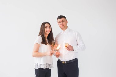 Yeni yıl, tatiller, tarih ve sevgililer günü konsepti - Beyaz arka plan üzerinde kıvılcımLar ışık ve şampanya bardak tutan Loving çift