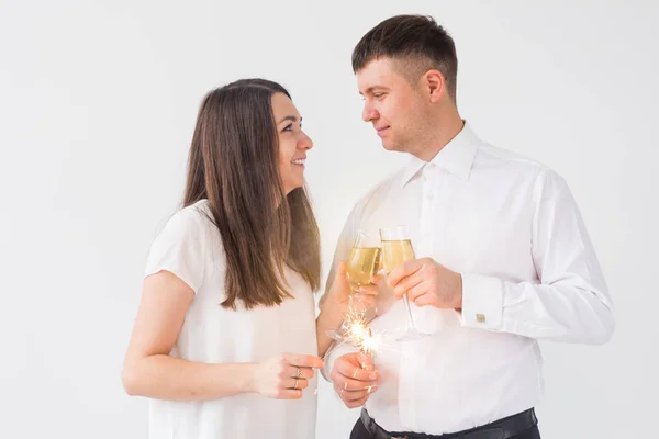 Ano Novo, feriados, data e dia dos namorados conceito - casal amoroso segurando faíscas luz e copos de champanhe sobre fundo branco — Fotografia de Stock