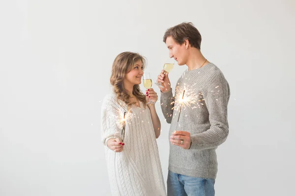 Ano Novo, feriados, data e dia dos namorados conceito - casal amoroso segurando faíscas luz e copos de champanhe sobre fundo branco — Fotografia de Stock