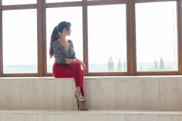 Ονειροπόληση, σκέψη και μοναξιά έννοια-νεαρή καυκάσια γυναίκα κάθεται στο σαλόνι της και κοιτάζοντας έξω από το μεγάλο παράθυρο — Φωτογραφία Αρχείου