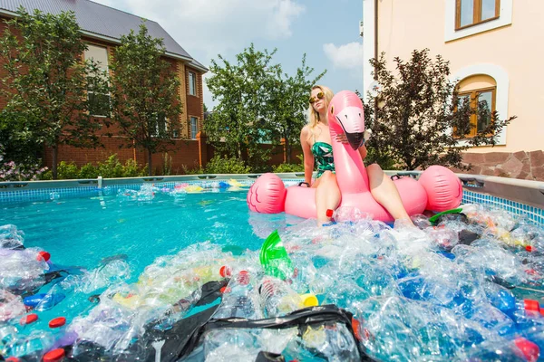 Çöp sorunu, plastik geri dönüşüm, kirlilik ve çevre kavramı - aptal kadın yüzer ve kirli bir havuzda eğlenin. Şişeler ve plastik torbalar onun yanında yüzer.