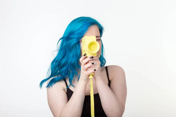 Люди, мода и мода - девушка с синими волосами держит желтую ретро-камеру на белом фоне — стоковое фото