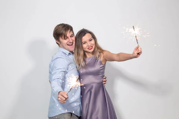 Conceito de festa, família e feriados - jovem casal segurando sparklers no fundo branco — Fotografia de Stock