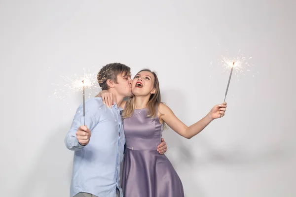 Festa, celebração, evento e feriados conceito - Homem segurando sparklers e beijo mulher com lábios vermelhos na bochecha — Fotografia de Stock