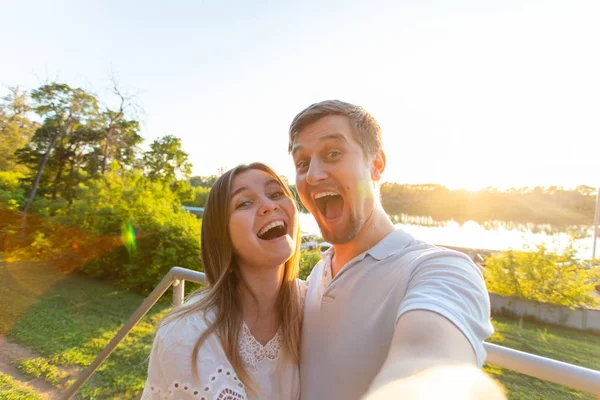 Capturar momentos brilhantes. Joyful jovem engraçado casal amoroso fazendo selfie na câmera enquanto está de pé ao ar livre — Fotografia de Stock