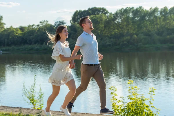 Liebes- und Beziehungskonzept - der glückliche Mann und die glückliche Frau beim Laufen in einem Park am See — Stockfoto