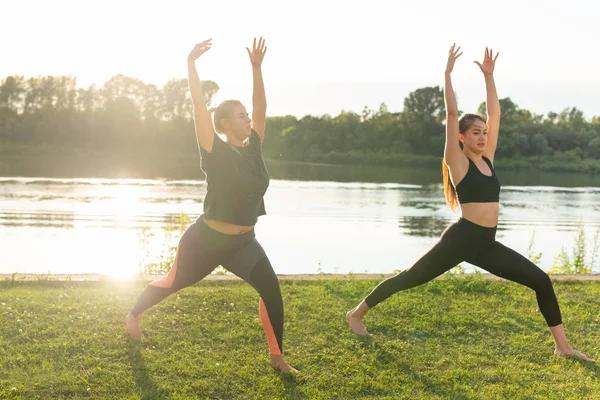 Female friends enjoying relaxing yoga outdoors in the park.