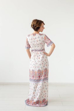 Beyaz bir duvara karşı duran uzun desenli elbiseli genç ince bir kadının arka görünümü. Sipariş için benzersiz ürünler kavramı