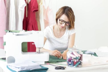 Üniversitede bir giysi tasarımcısı genç güzel kız öğrenci çalışma ve bir dikiş makinesi ile bir masada oturan ilk tezyapar. Giyim tasarım konsepti.