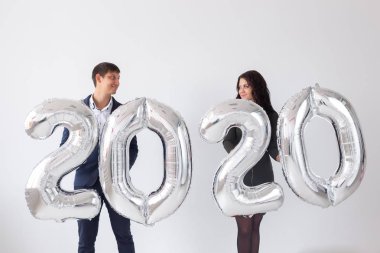 Yeni yıl, kutlama ve tatil konsepti - beyaz arka plan üzerinde yeni yıl için gümüş balonlardan yapılmış 2020 işareti ile eğlenen aşk çift