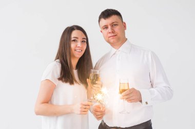 Yeni yıl, tatiller, tarih ve sevgililer günü konsepti - Beyaz arka plan üzerinde kıvılcımLar ışık ve şampanya bardak tutan Loving çift