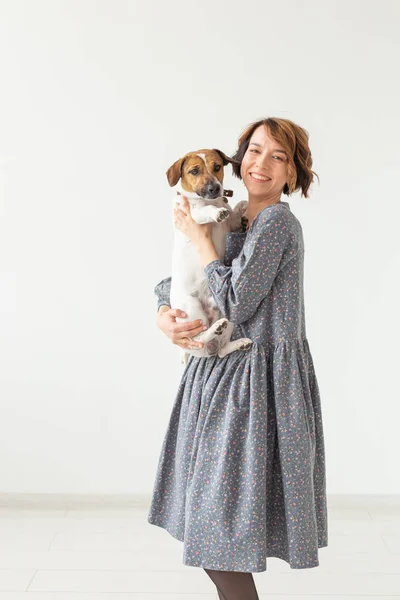 Encantadora joven sonriente con un elegante vestido gris sosteniendo a su perro favorito Jack Russell Terrier. Concepto perros favoritos . — Foto de Stock