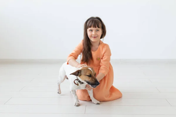 Concepto de propietario de niños y mascotas: niña pequeña sentada en el suelo con un lindo cachorro Jack Russell Terrier — Foto de Stock