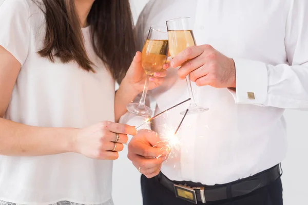 Anno nuovo, vacanze, data e concetto di giorno di San Valentino - Coppia amorevole che tiene scintille luce e bicchieri di champagne primo piano su sfondo bianco — Foto Stock