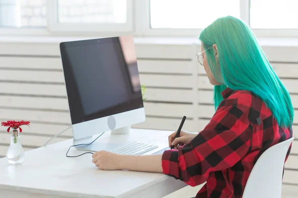 Business, designer and animator concept - young woman illustrator or artist with green hair draws on the graphic tablet, side view