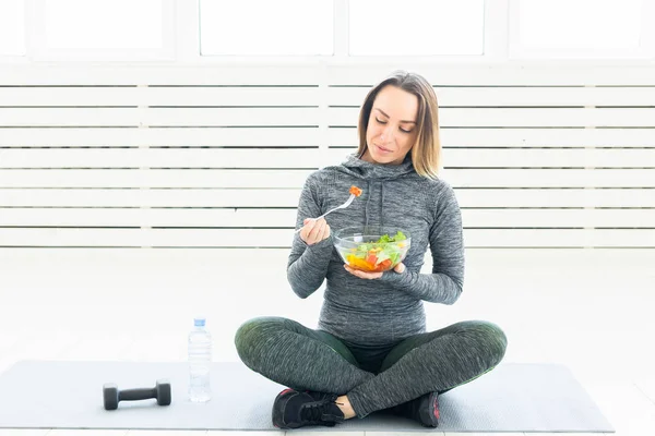 Deporte, estilo de vida saludable y concepto de personas: mujer joven con ensalada y una mancuerna sentada en el suelo — Foto de Stock