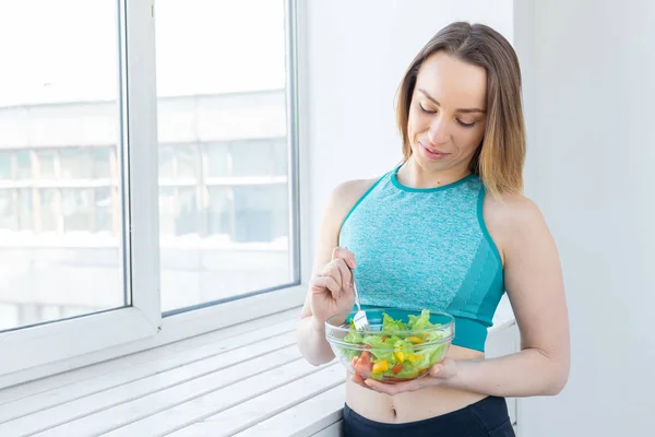 Stile di vita sano, fitness e dieta concetto - insalata alimentare e donna magra in abbigliamento sportivo vicino alla finestra — Foto Stock