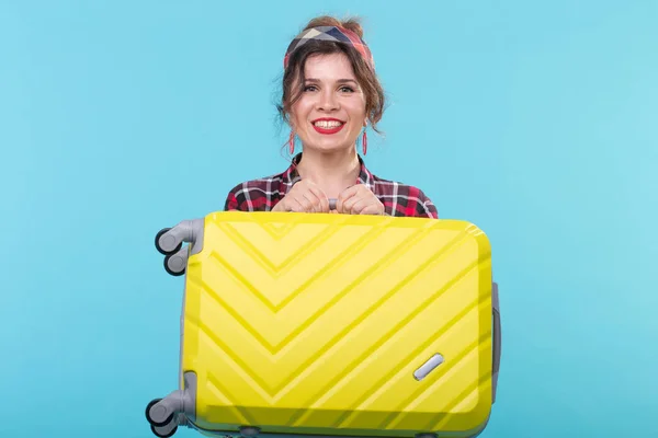 Jeune femme souriante positive dans une chemise à carreaux tenant une valise jaune posant sur un fond bleu. Concept de tourisme et de voyage — Photo