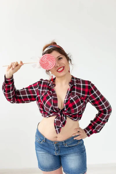 Muito sorrindo jovem mulher em uma camisa xadrez fecha o olho com grandes pirulitos coloridos e posando contra um fundo branco. Conceito de diversão e sobremesas . — Fotografia de Stock