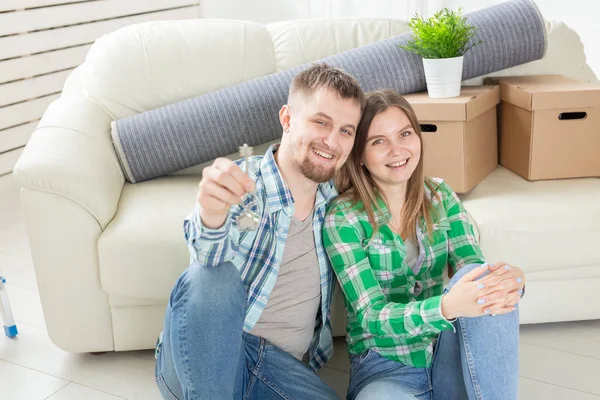 Charming young woman and her husband holding in hands the keys to their new apartment while sitting in her new living room. Housewarming and mortgage in new building concept