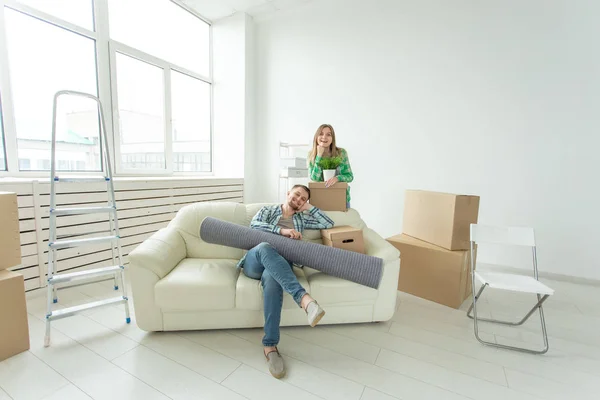 Nöjda glada ungt par stark man och vacker kvinna som håller sina saker i sina händer sitter i vardags rummet i en ny lägenhet. Inflyttnings konceptet. — Stockfoto