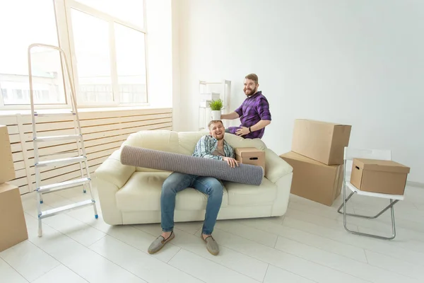 Два друга-студента мужчины держат свои вещи в руках, сидя в гостиной новой квартиры. Концепция новоселье — стоковое фото