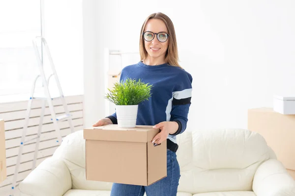 Jovem tem uma caixa e um pote de plantas enquanto se muda para um novo apartamento. Acolhimento e novo conceito de habitação . — Fotografia de Stock