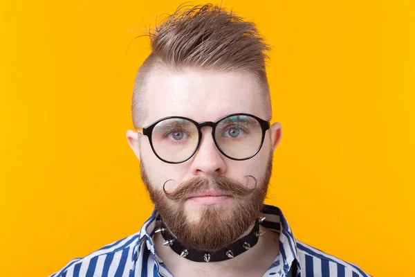 Joven hombre de moda positivo hipster con una barba bigote y collar fetiche en camisa posando sobre un fondo amarillo. Concepto de roca y subcultura . —  Fotos de Stock