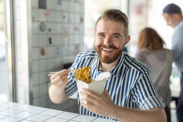 Positieve jonge stijlvolle kerel die Chinese noedels eet in een café tijdens een pauze op het werk. Het concept van rust en gezonde snack. — Stockfoto