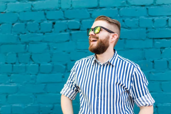 青い壁に向かってポーズをとる口ひげとあごひげを持つメガネをかけた陽気なポジティブなスタイリッシュな学生の肖像画。成功する陽気な人々の概念. — ストック写真