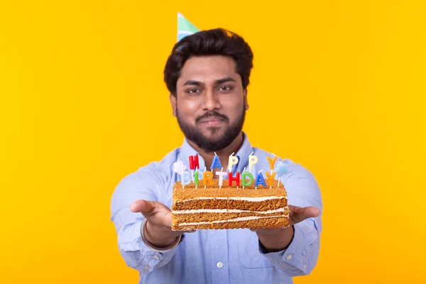 Engraçado cara positivo segura em suas mãos um bolo caseiro com a inscrição feliz aniversário posando em um fundo amarelo. Conceito de feriados e aniversários . — Fotografia de Stock