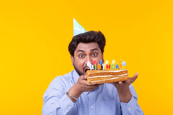 Engraçado cara positivo segura em suas mãos um bolo caseiro com a inscrição feliz aniversário posando em um fundo amarelo. Conceito de feriados e aniversários . — Fotografia de Stock