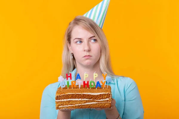 Komik pozitif genç kadın elinde sarı bir arka plan üzerinde poz yazıt mutlu doğum günü ile ev yapımı bir pasta tutar. Tatil ve yıldönümleri kavramı. — Stok fotoğraf