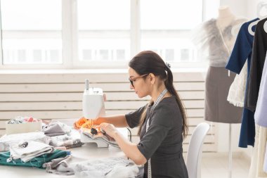 İnsanlar ve moda kavramı - genç terzi kadın dikiş makinesi giysilerini diker.
