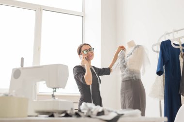 Terzi, terzi, moda ve showroom konsept - güzel genç tasarımcı cep telefonda konuşurken ve terzilik stüdyo işinde incelenirken gülümseyen
