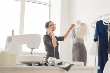 Terzi, terzi, moda ve showroom konsept - güzel genç tasarımcı cep telefonda konuşurken ve terzilik stüdyo işinde incelenirken gülümseyen