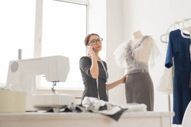 Terzi, terzi, moda ve showroom konsept - güzel genç tasarımcı cep telefonda konuşurken ve terzilik stüdyo işinde incelenirken gülümseyen