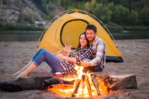People, tourism and nature concept - Man embrace woman sitting near a fire