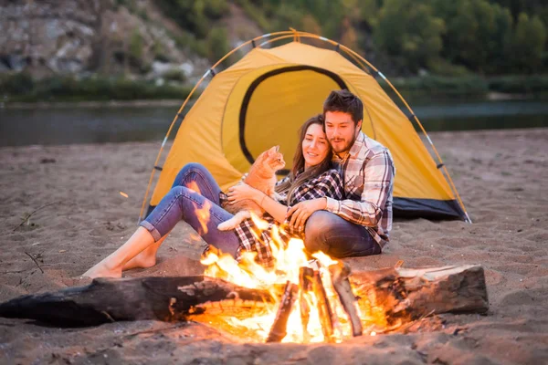 People, tourism and nature concept - Man and woman with their cat sit near a fire — Stock Photo, Image