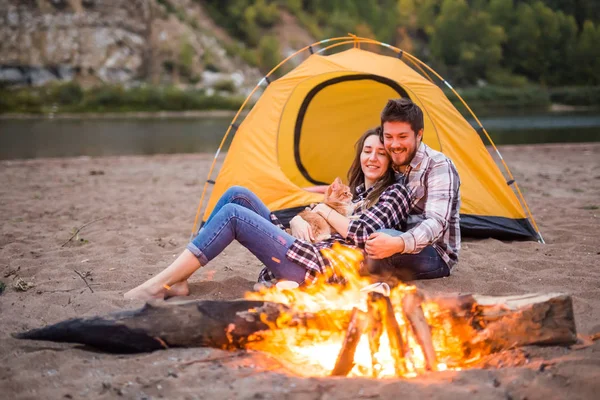People, tourism and nature concept - Romantic evening, man embrace woman sitting near a campfire