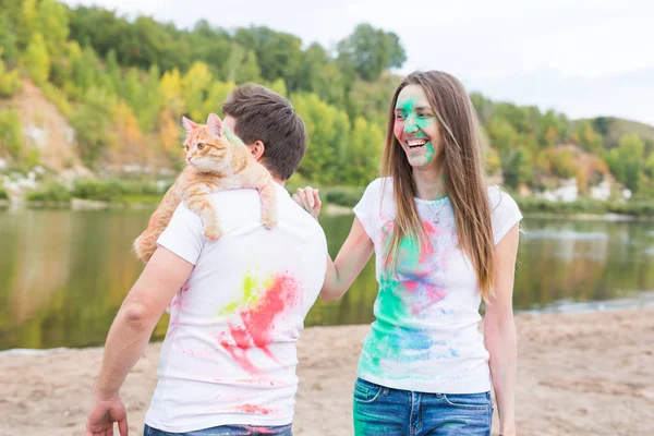 Animali domestici, turismo estivo, festival holi e concetto di natura - divertente uomo e donna con gatto su sfondo naturale — Foto Stock