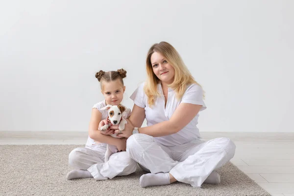 Personer, familj och husdjur koncept - mor och dotter som sitter på golvet med valp Jack Russell Terrier — Stockfoto