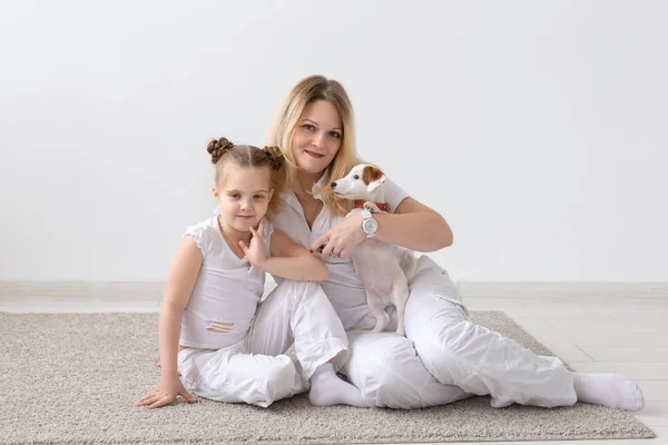 Concept famille et animaux de compagnie - mère et fille enfant assis sur le sol avec chiot Jack Russell Terrier sur fond de chambre blanche — Photo