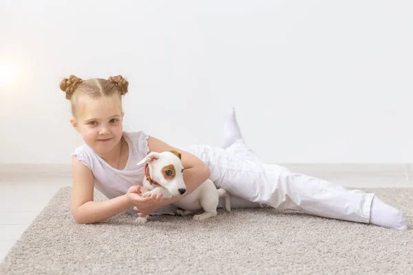 people, children and pets concept - little child girl lying on the floor with cute puppy Jack Russell Terrier