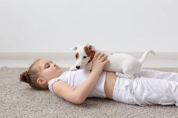 Pessoas, crianças e conceito de animais de estimação - menina criança deitada no chão com filhote de cachorro bonito nas mãos — Fotografia de Stock