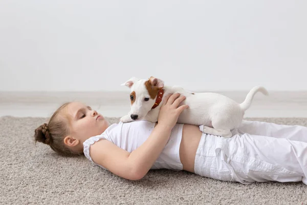 people, children and pets concept - little kid girl lying on the floor with cute puppy in hands