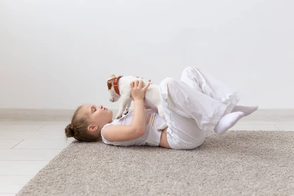 Persone, bambini e animali domestici concetto - bambina sdraiata sul pavimento con cucciolo carino Jack Russell Terrier — Foto Stock