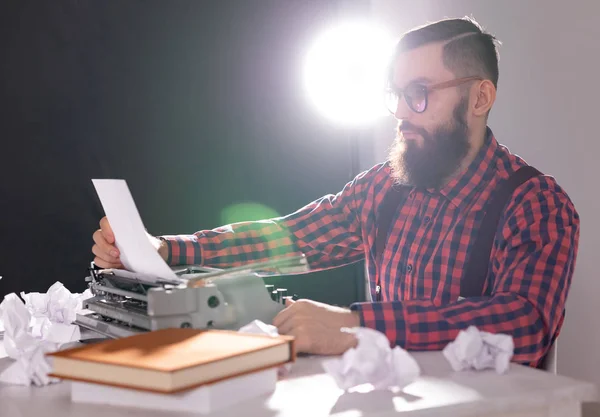 Gente y concepto de tecnología - Día Mundial del escritor, hombre guapo con barba trabajando en la máquina de escribir sobre fondo negro — Foto de Stock