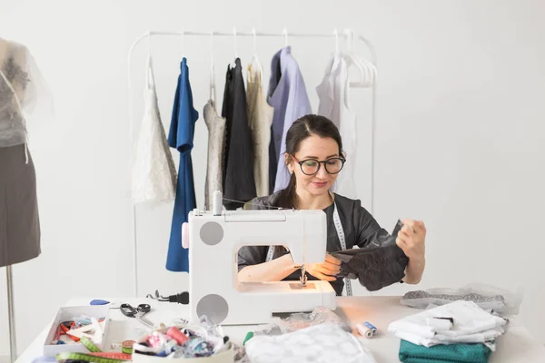 服装制造商、裁缝和时尚概念--微笑着的女性时尚设计师使用缝纫机, 坐在办公桌后 — 图库照片