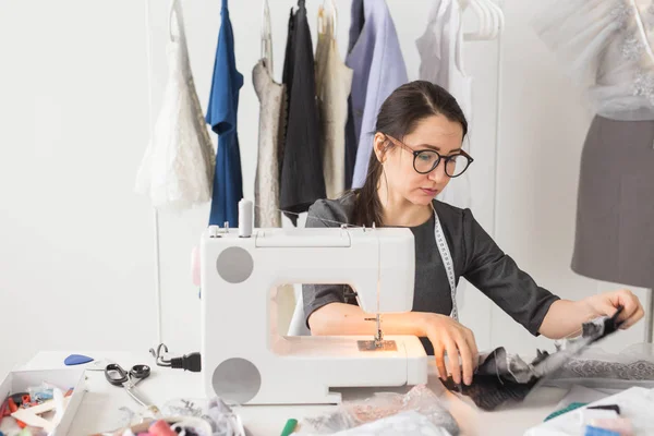 Dressmaker, tailleur et concept de mode - Créatrice de mode souriante utilisant une machine à coudre et assise derrière son bureau — Photo